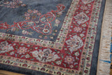 Laristan carpet corner featuring cherry red floral border, dusty blue field, and ivory fringe.