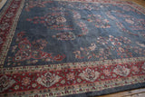 Vintage Laristan carpet's ornate cherry red border, floral motifs on dusty denim field.