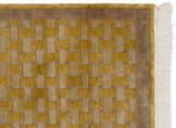 Close-up of vintage Indian rug corner, highlighting carved saffron gold and beige basket weave with white fringe.