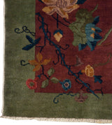 Nichols Art Deco rug's celadon green border, burgundy field, floral vines, and ivory fringe.