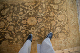 Looking down at the soft, lustrous pile and olive floral pattern of a gold Oushak rug.