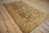 A gold wash Indian Oushak rug viewed from an angle, showing its olive floral details and ivory fringe.