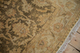 A close-up of the Oushak rug's plush pile, highlighting the gold and olive floral border and ivory fringe.
