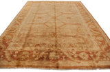 Angled view of a lustrous gold wash Oushak carpet with a rust and copper vine border.