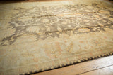 Charcoal floral field and dusty gold palmette border of the Indian Oushak carpet.