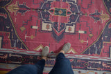 A top-down perspective on the flat weave texture of a raspberry and navy blue vintage Dhurrie.
