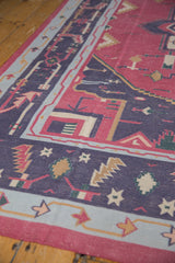 Angled detail of the vintage Dhurrie's hand woven texture and geometric border in raspberry and navy blue.