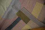 Folded corner of a contemporary Kilim rug, revealing flatweave texture and abstract mauve, blue, bronze forms.