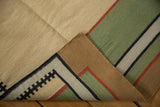 Curled edge of vintage kilim, showing hand-woven flat-weave and geometric patterns in sand, green, red, black.