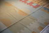 Overlapping geometric shapes in beige, pale gold, and slate blue on the kilim.