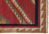 Soumac rug corner showing sharp serrated patterns in red, ivory, green, black, with fringe.