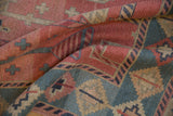 Geometric patterns of a hand-woven Soumac carpet in dusty rose and sea foam green.