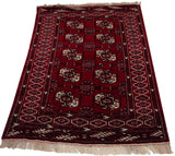 Corner of a vintage Yomud rug, showcasing cherry red shield motifs, geometric border, and ivory fringe.