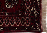 Vintage Yomud rug corner with cherry red geometric shield motifs, charcoal details, and fringe.