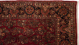 Corner of a vintage American Sarouk carpet showing the intricate navy blue floral border and ruby red field.