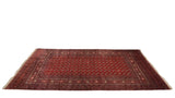 Angled perspective of a vintage Bokhara carpet showing the sheen on its plush red field of gul medallions.