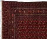 Corner of a vintage Bokhara rug showing intricate geometric borders, a red gul medallion field, and ivory fringe.