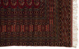 Detailed corner of a vintage Bokhara carpet showing intricate geometric borders and intact ivory fringe.