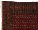 The finely woven corner of a vintage Bokhara carpet, detailing the geometric borders and ivory fringe.