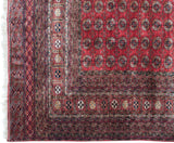Corner detail of vintage Bokhara rug featuring cherry red gul medallions and rich geometric borders.