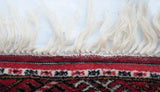 Knotted cream fringe and cherry red geometric pattern on a vintage Bokhara rug.
