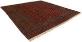 Angled view of a vintage Bokhara square carpet showing its cherry red field and complex geometric borders.