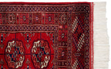 Fine weave cherry red Bokhara rug corner with geometric patterns, intact selvage, and cream fringe.