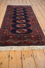 Fine weave detail of Bokhara rug's navy field, deep rust gul medallions, and ivory fringe.