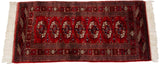Cherry red Bokhara runner with geometric gul medallions, patterned borders, and ivory fringe.