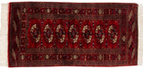 Plush cherry red Bokhara rug corner with gul motifs and intact white fringe.