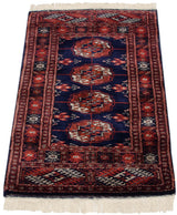 Lustrous pile of a vintage Bokhara rug with repeating gul medallions in rust on an indigo field.