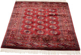 Plush wine red Bokhara rug corner with navy gul medallions, geometric border, and white fringe.
