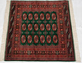Overhead view of a vintage Bokhara rug with a green field and symmetrical rust-colored guls.