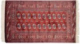 Multi-column rows of geometric gul medallions on a lustrous wine-red Bokhara rug.