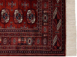 The finely woven corner of a vintage Bokhara rug, showing intricate borders and clean white fringe.