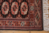Corner of a vintage Bokhara rug highlighting its detailed geometric border and original white fringe.
