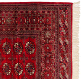 Detailed corner of a vintage Bokhara rug with intact side cord, geometric borders, and clean ivory fringe.
