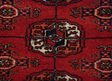 A detailed gul medallion in navy and ivory on the dense, brick-red pile of a fine Bokhara rug.