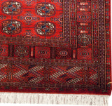 Corner detail of a fine Bokhara runner with plush red wool, intricate borders, and ivory fringe.