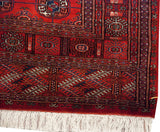 Corner detail of a fine Bokhara rug with plush pile, geometric guls, and ivory fringe.