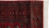 Corner of a vintage Bokhara runner showing the detailed border, intact side cord, and ivory fringe.