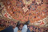 Boots on a vintage Indian Heriz rug, showcasing rust field and navy floral border detail.
