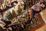 Rolled vintage Indian Heriz rug edge displays thick pile, navy, rust, ivory arabesques.