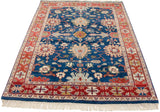 Angled view of a vintage Indian rug with a sapphire blue field and terracotta floral border.