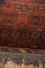 Corner view showing the Afghani Bokhara rug's charcoal fringe, kilim end, and plush rust pile.