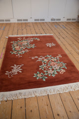 Copper Art Deco rug showing celadon, mauve, ivory floral sprays, and white fringe.