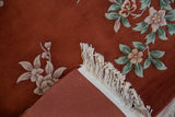Vintage Art Deco rug corner reveals copper field, celadon florals, white fringe, hand-knotted back.