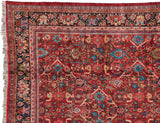 Corner of a vintage Mahal carpet showing the charcoal navy floral border against the ruby red, gem-toned lattice field.