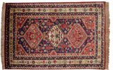 Geometric animal, bird, and Cyprus tree motifs on the rug's indigo blue field.