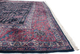 Angled view of the vintage Sarouk's cochineal red border alongside its deep indigo floral field.